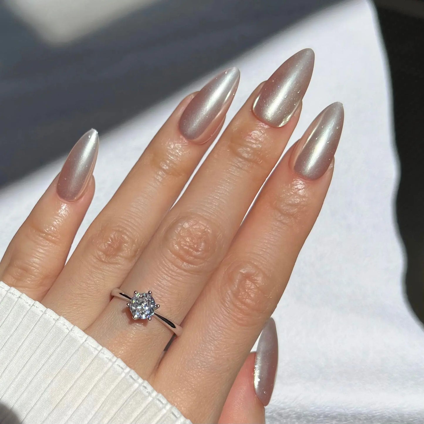 A hand showcasing reflective silver press-on nails with a high-gloss, mirror-like surface, perfect for a striking and elegant style.