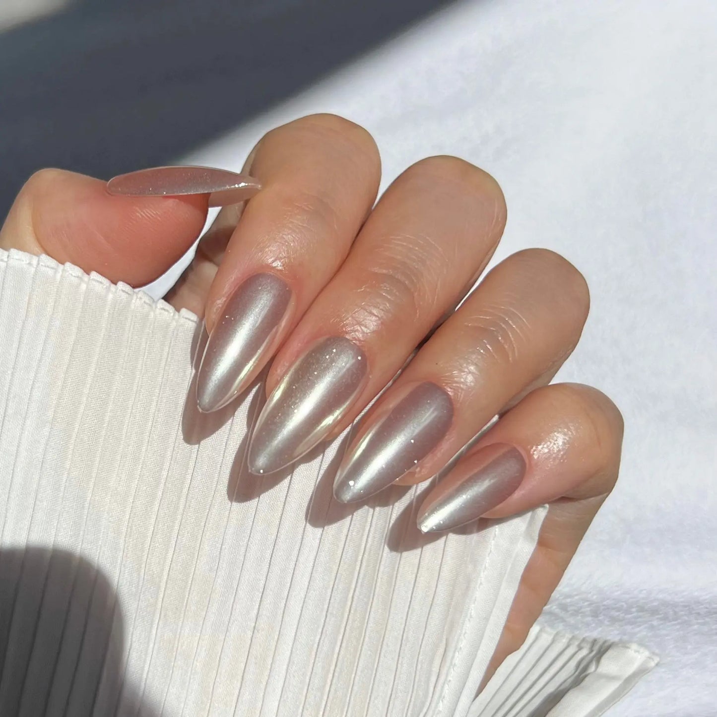 A close-up of a hand wearing almond-shaped nails with a shiny silver mirror finish, offering a modern and glamorous appearance.