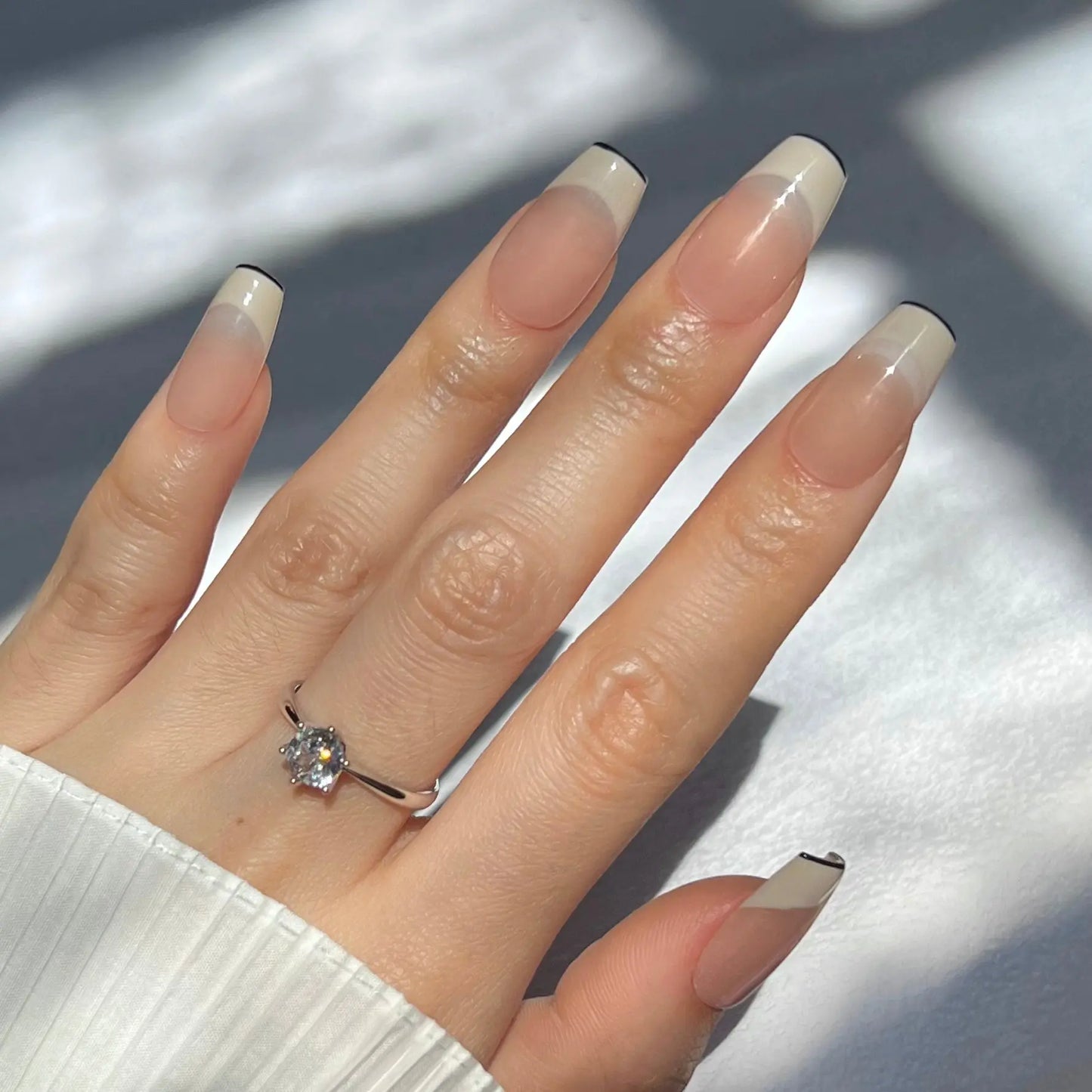 A hand showcasing press-on nails with nude bases and chic black tips, perfect for a refined yet stylish appearance.
