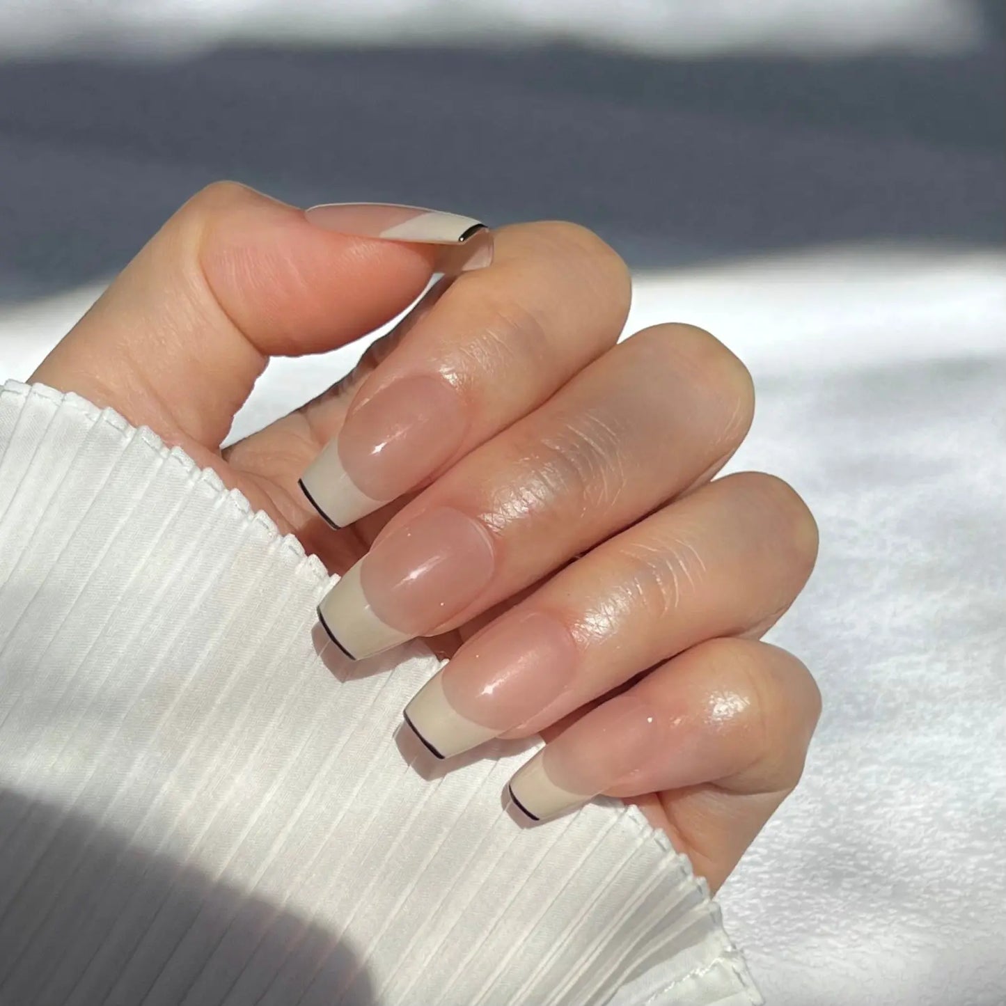 A close-up of a hand wearing square-shaped press-on nails with nude bases and bold black tips, offering a sophisticated and contemporary look.
