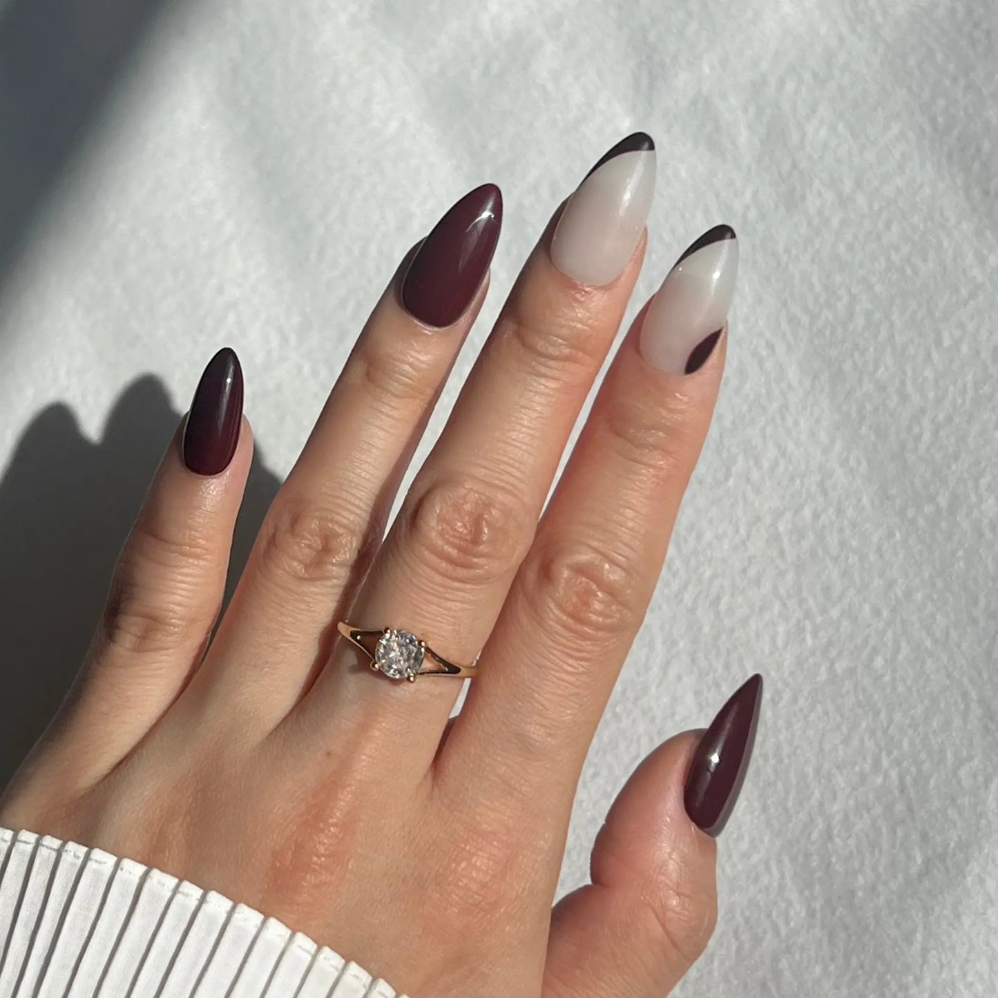 A hand showcasing press-on nails with deep burgundy hues and ripple accents, offering a bold and unique style.