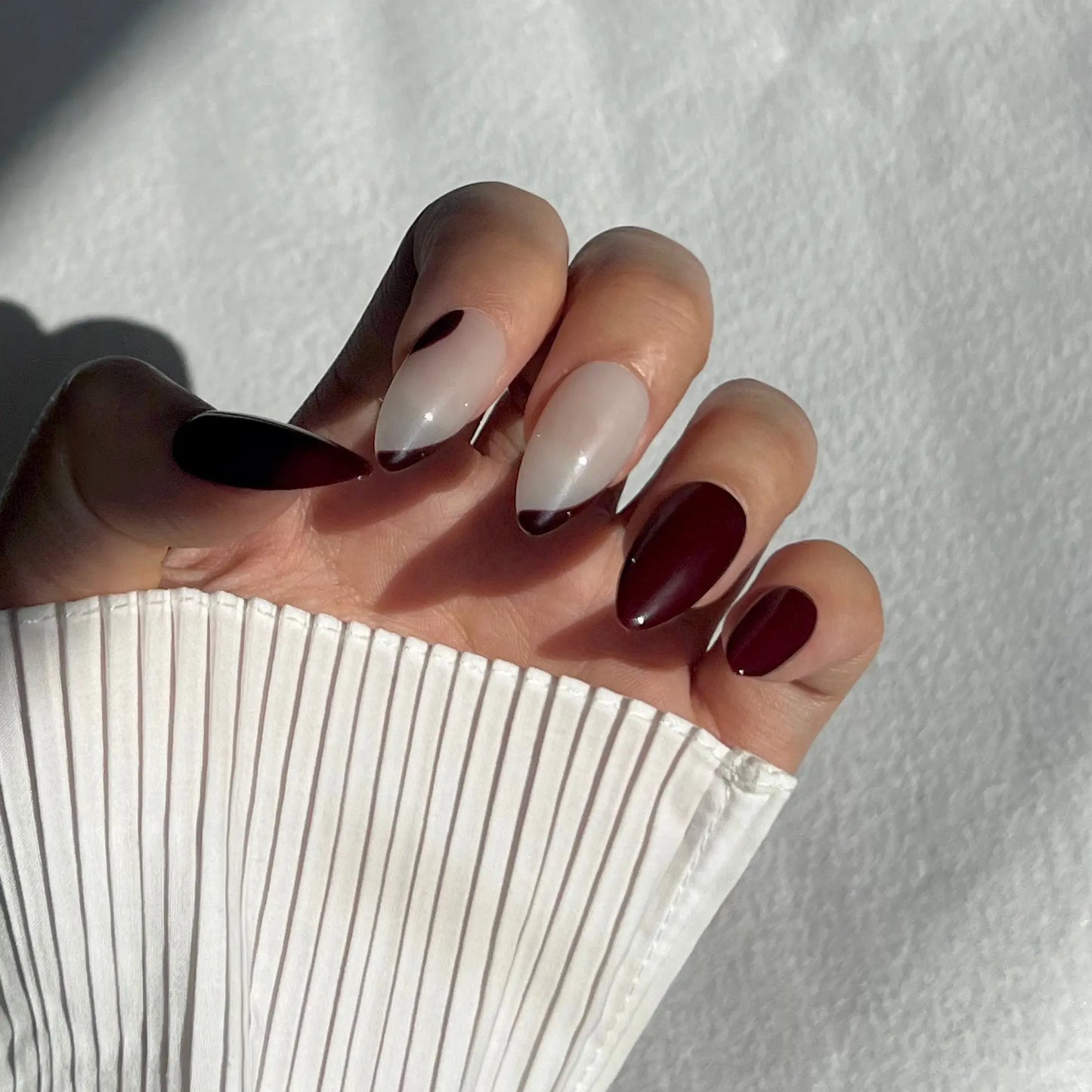 A close-up of a hand wearing almond-shaped press-on nails with rich burgundy and ripple designs, perfect for a striking and mysterious appearance.