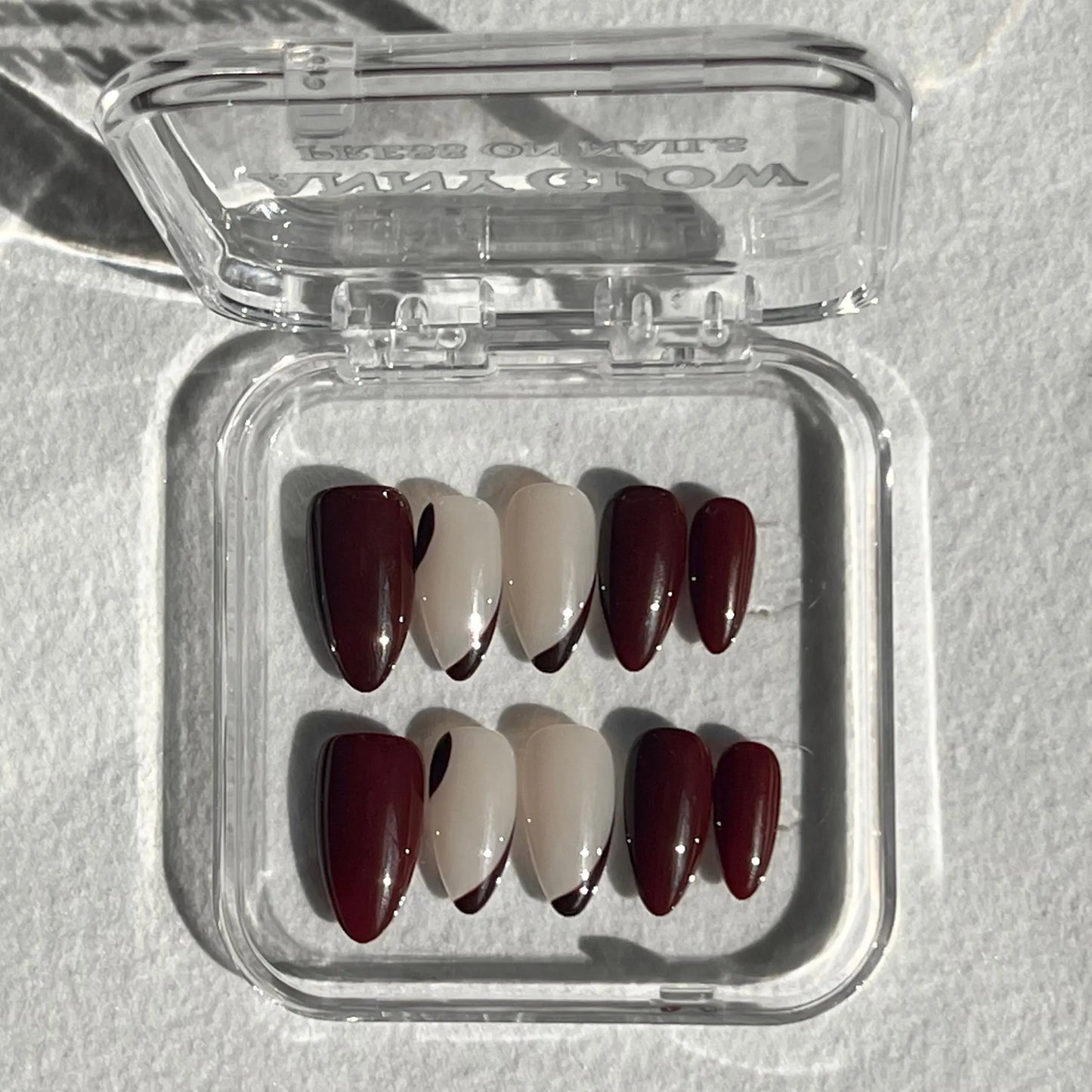 A set of press-on nails displayed in a clear plastic box, featuring a deep burgundy color with bold ripple patterns for a dramatic and elegant look.