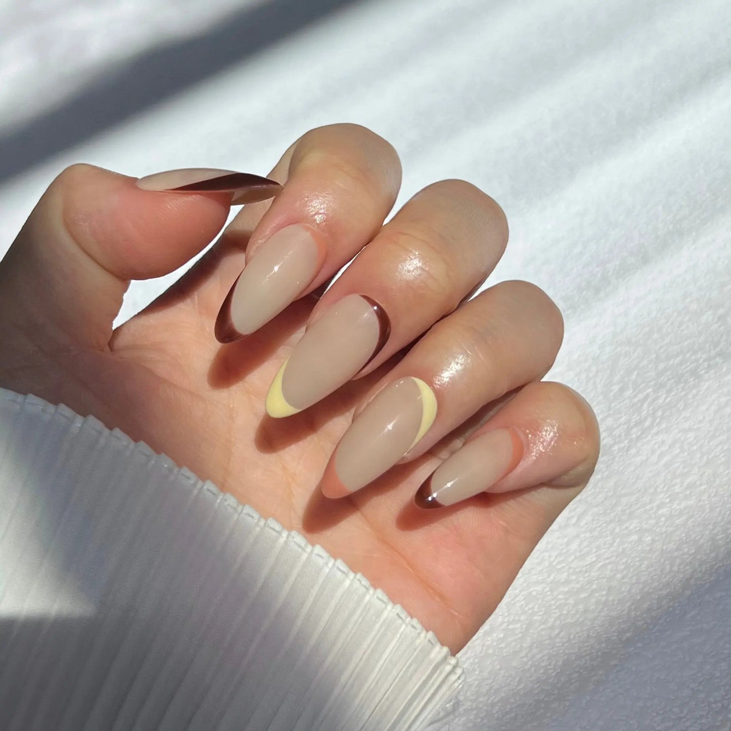 A close-up of a hand wearing almond-shaped press-on nails in gradient cappuccino tones, showcasing a polished and chic appearance.