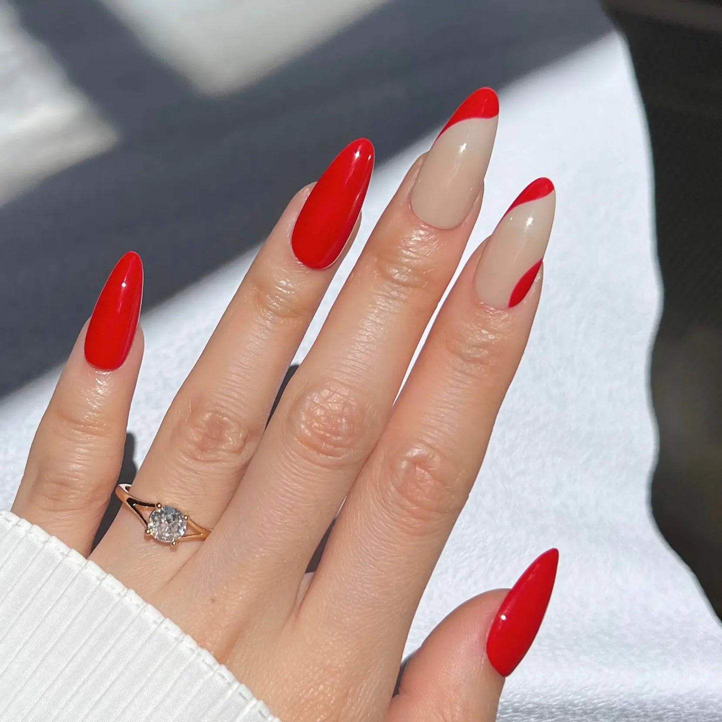 A hand showcasing glossy red press-on nails with nude wave details, offering a striking yet refined style.