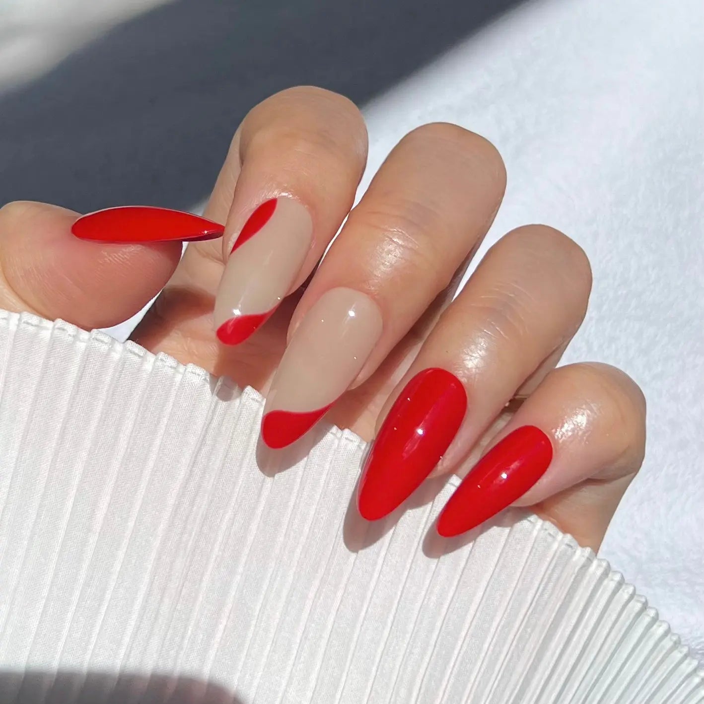 A close-up of a hand wearing almond-shaped press-on nails with a bold red color and nude wave accents, perfect for a chic and elegant look.