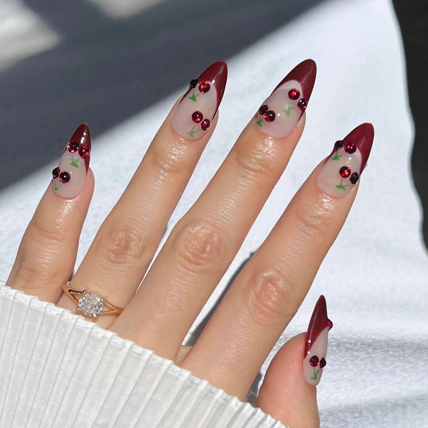 A hand showcasing press-on nails with red tips and glittering cherry accents, perfect for a playful and whimsical style.