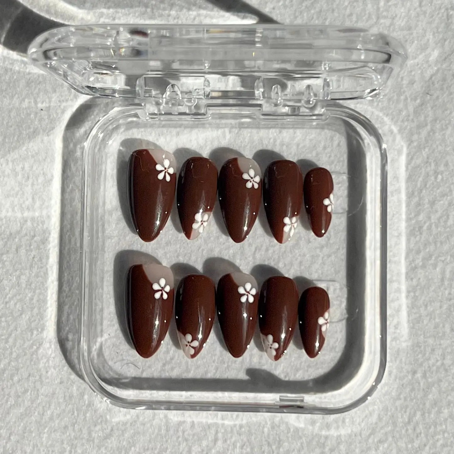 A set of press-on nails displayed in a clear plastic box, featuring a rich earthy tone with subtle sparkle, adding a hint of glamour.