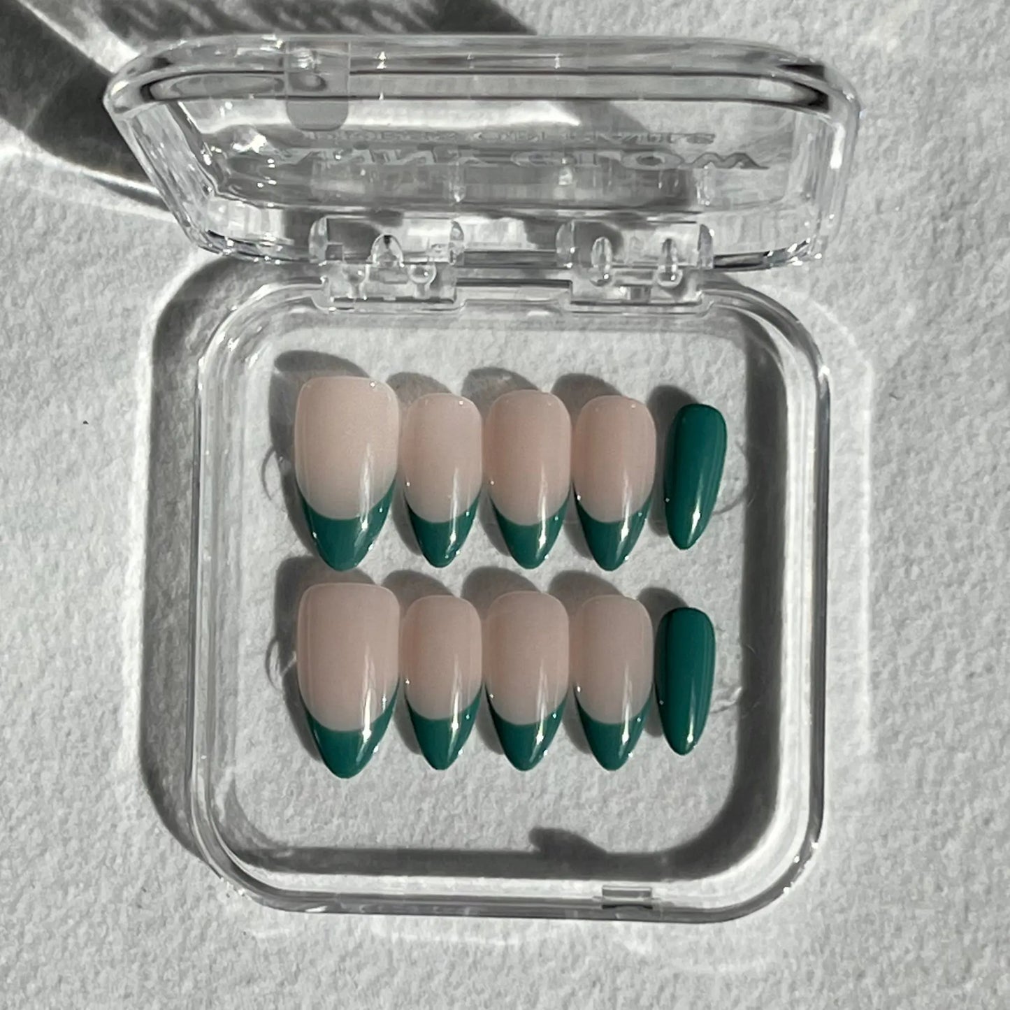 A set of press-on nails in a clear plastic box, featuring a soft nude base with jade green tips, creating a bold yet sophisticated look.