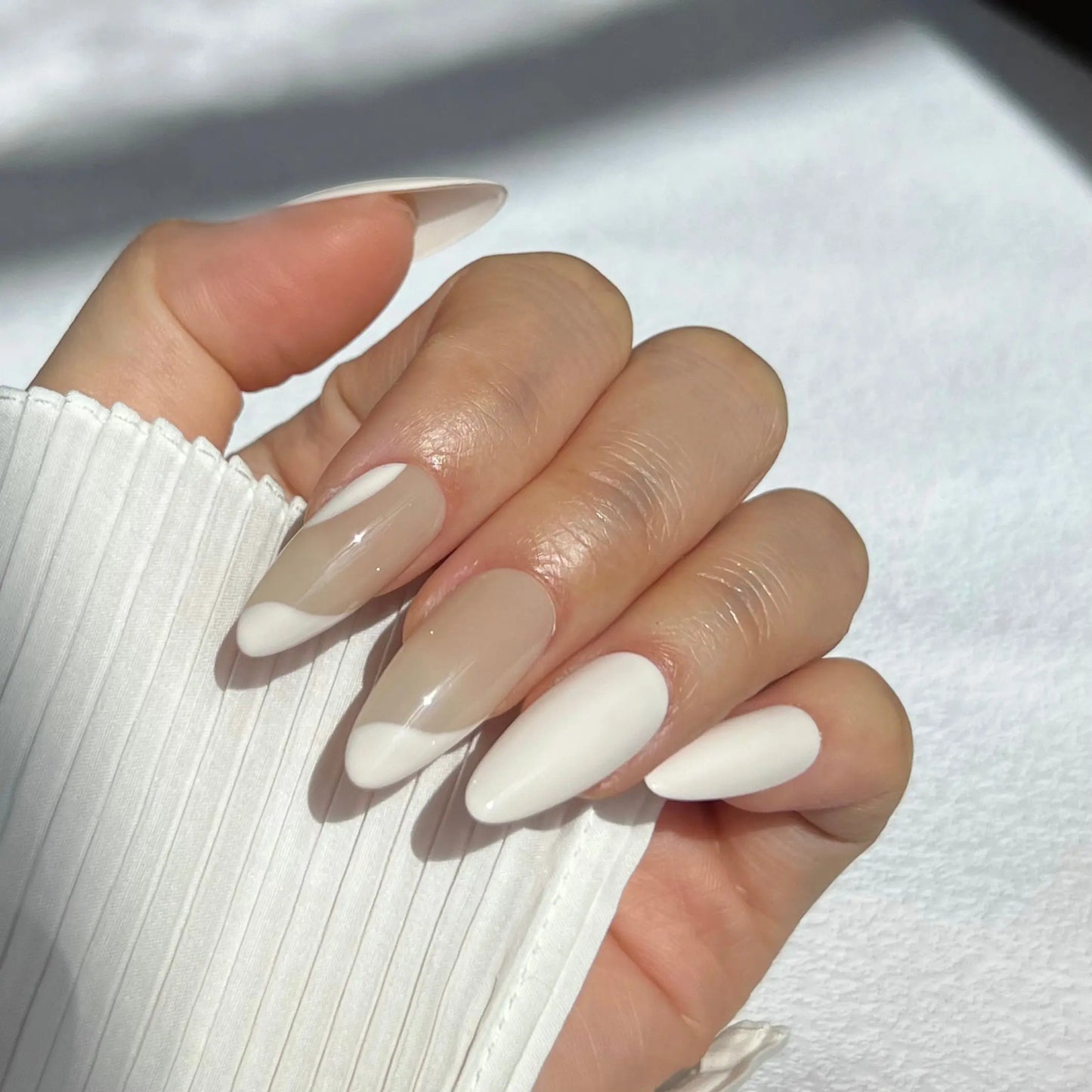 A close-up of a hand wearing almond-shaped press-on nails with a smooth ivory finish and translucent nude accents for an elegant, minimal look.