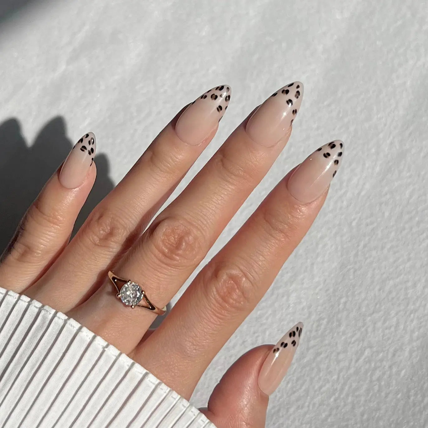 A hand showcasing press-on nails with a nude base and leopard print detailing, offering a fashionable and edgy appearance.