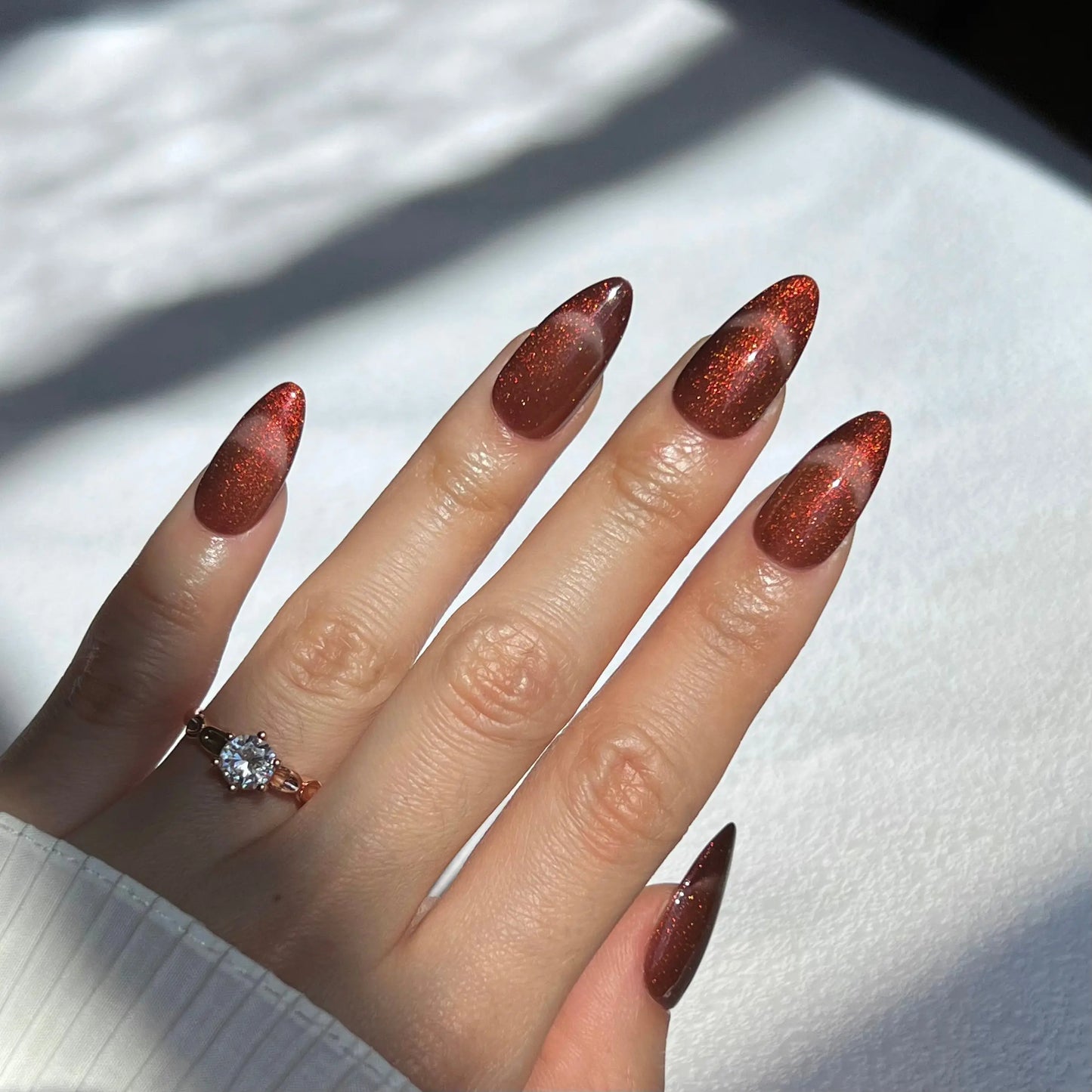 A hand showcasing deep red glittering press-on nails, reflecting light for a striking and elegant style.