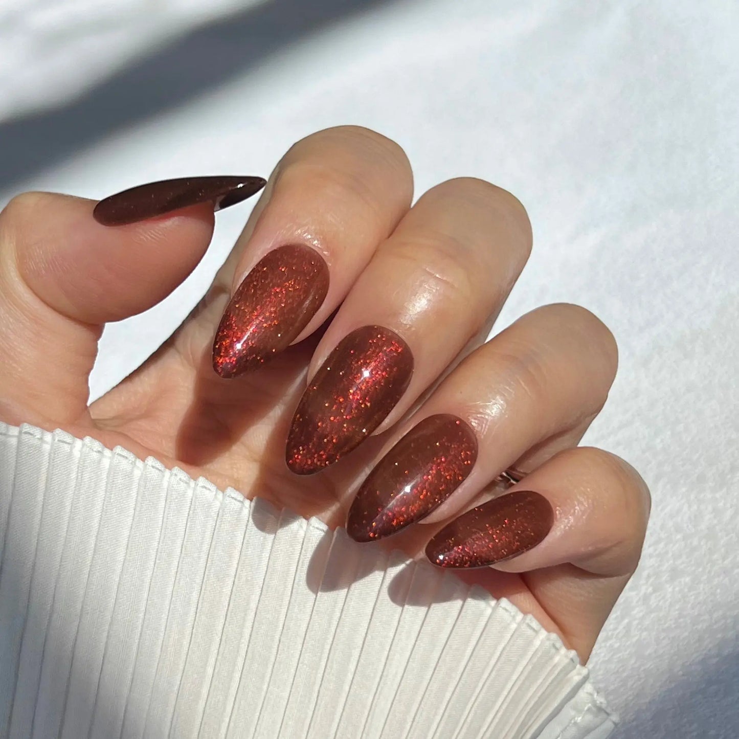 A close-up of a hand wearing almond-shaped press-on nails in a rich red color with glittery accents, offering a luminous and glamorous appearance.