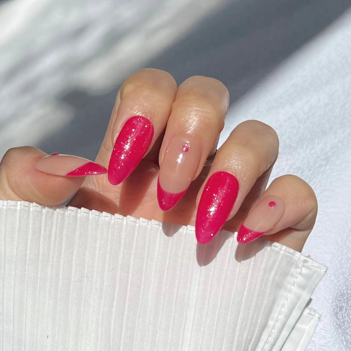 A close-up of a hand wearing almond-shaped magenta press-on nails, featuring a shiny, glittering surface for a lively and striking appearance.