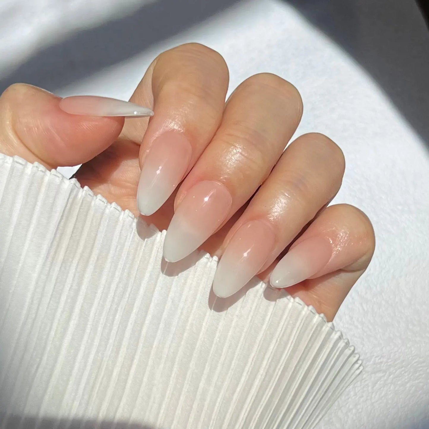 A close-up of a hand wearing almond-shaped press-on nails in a subtle peach shade, offering a sleek and natural appearance.