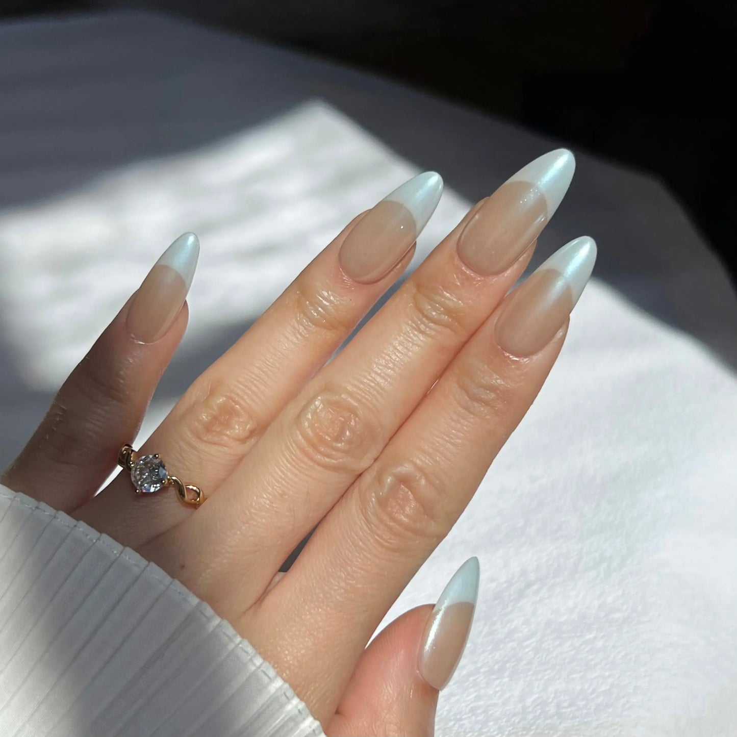 Another view of a hand showcasing the Santorini Press On Nails with pastel blue tips and a nude base, highlighting the shimmer and graceful almond shape.