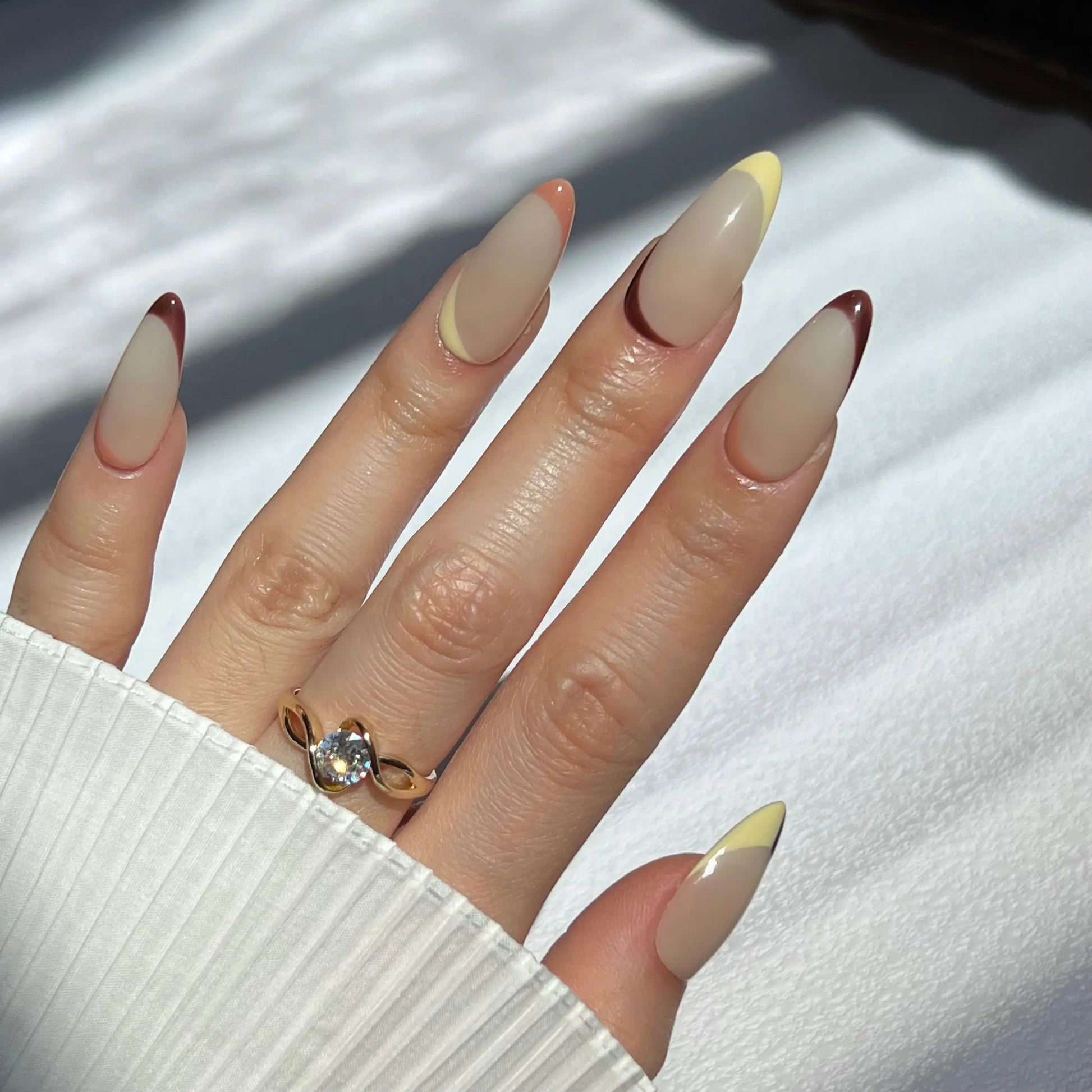 A hand showcasing soft beige and brown-toned press-on nails with a glossy finish, perfect for a sophisticated and refined style.