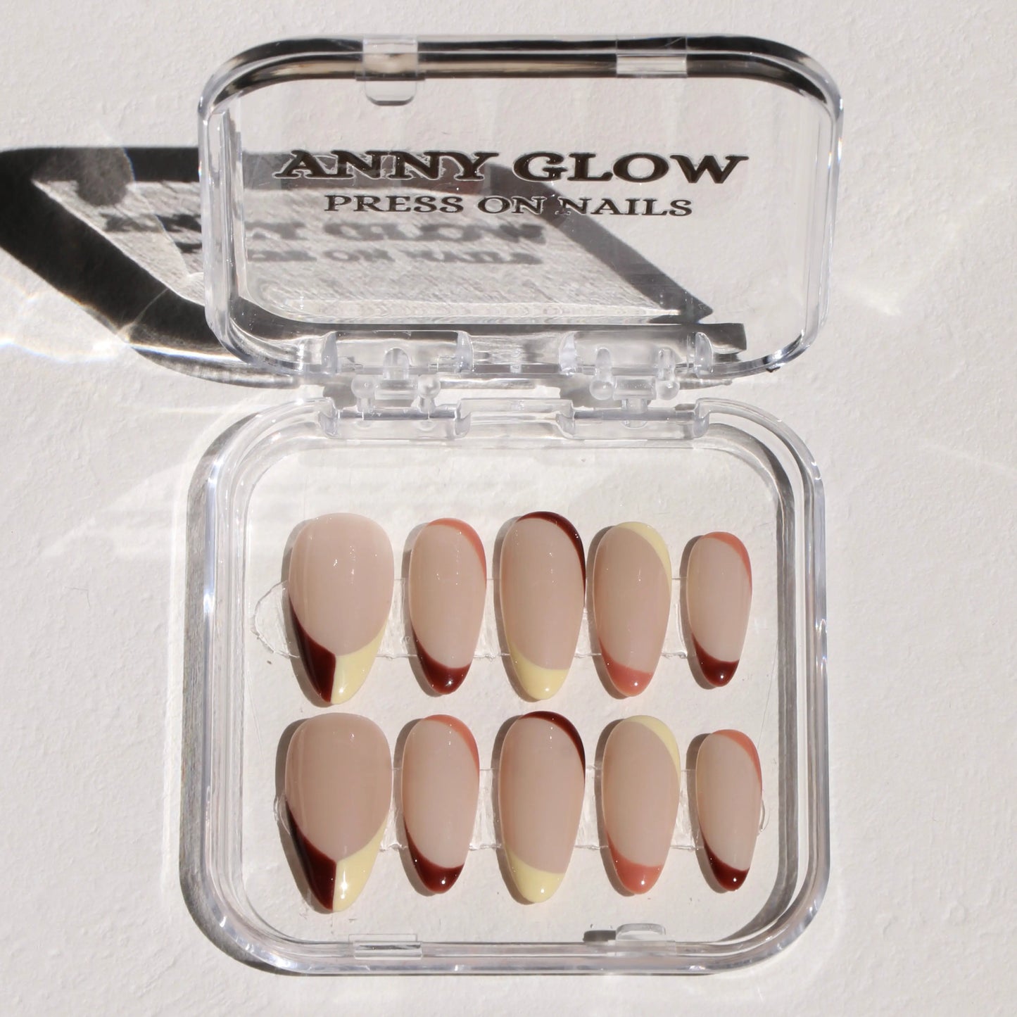A set of press-on nails displayed in a clear plastic box, featuring warm cappuccino-toned shades with soft beige and creamy brown hues for an elegant, minimalist look.