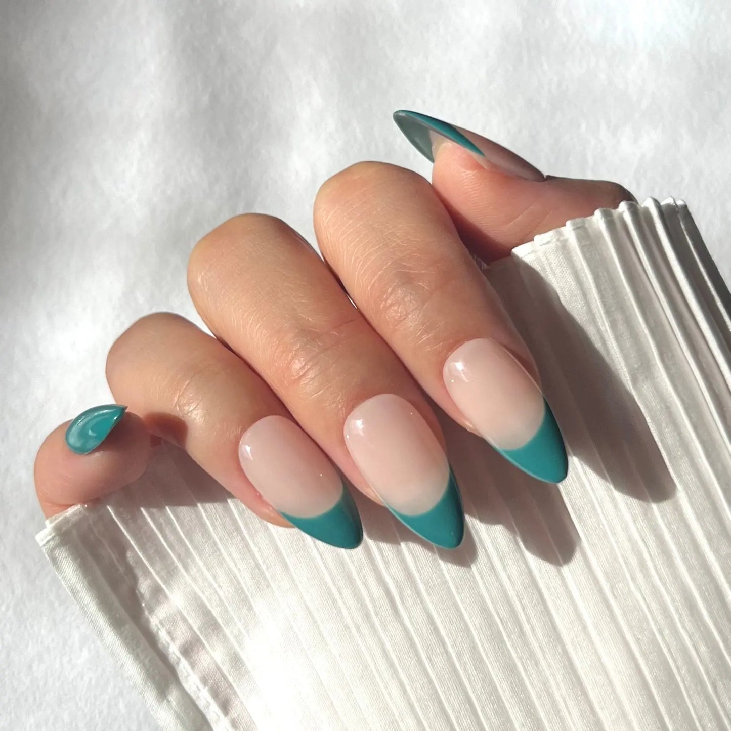 A close-up of a hand wearing almond-shaped press-on nails with jade green tips and a nude base, offering a chic and elegant style.