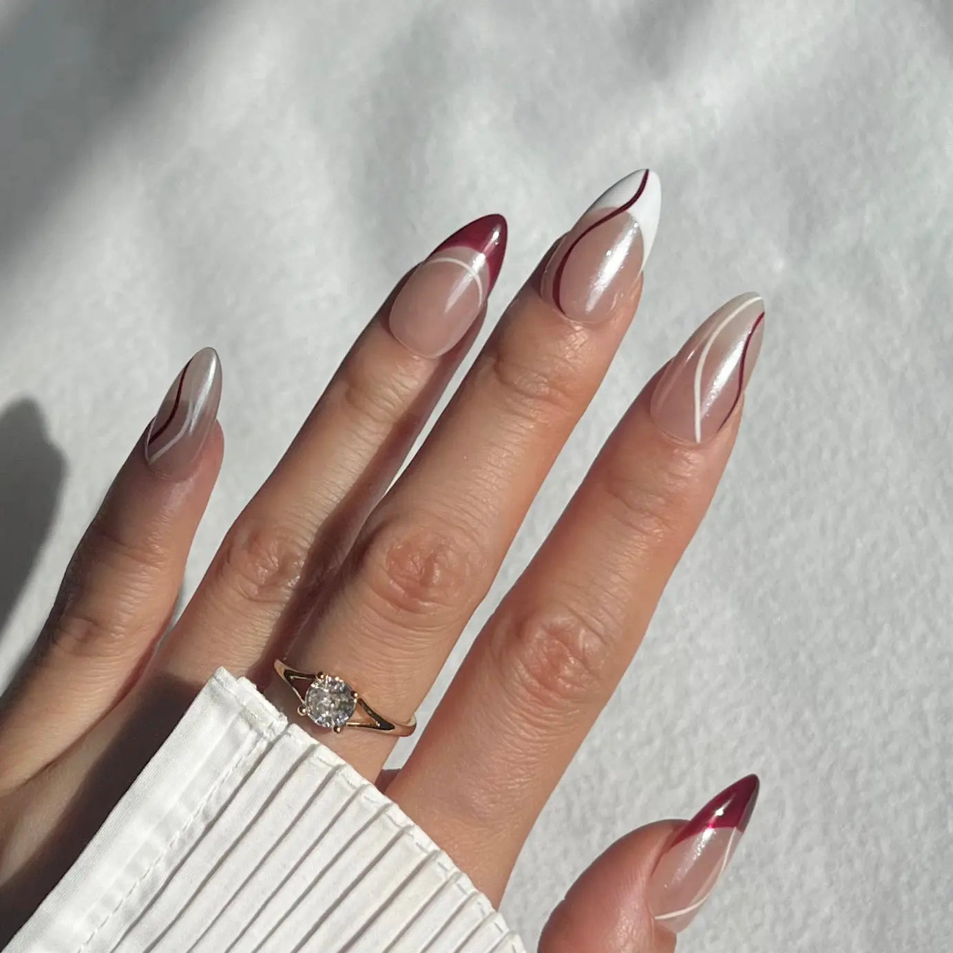 A hand showcasing press-on nails with minimalist burgundy and white line details, perfect for a sleek and elegant appearance.