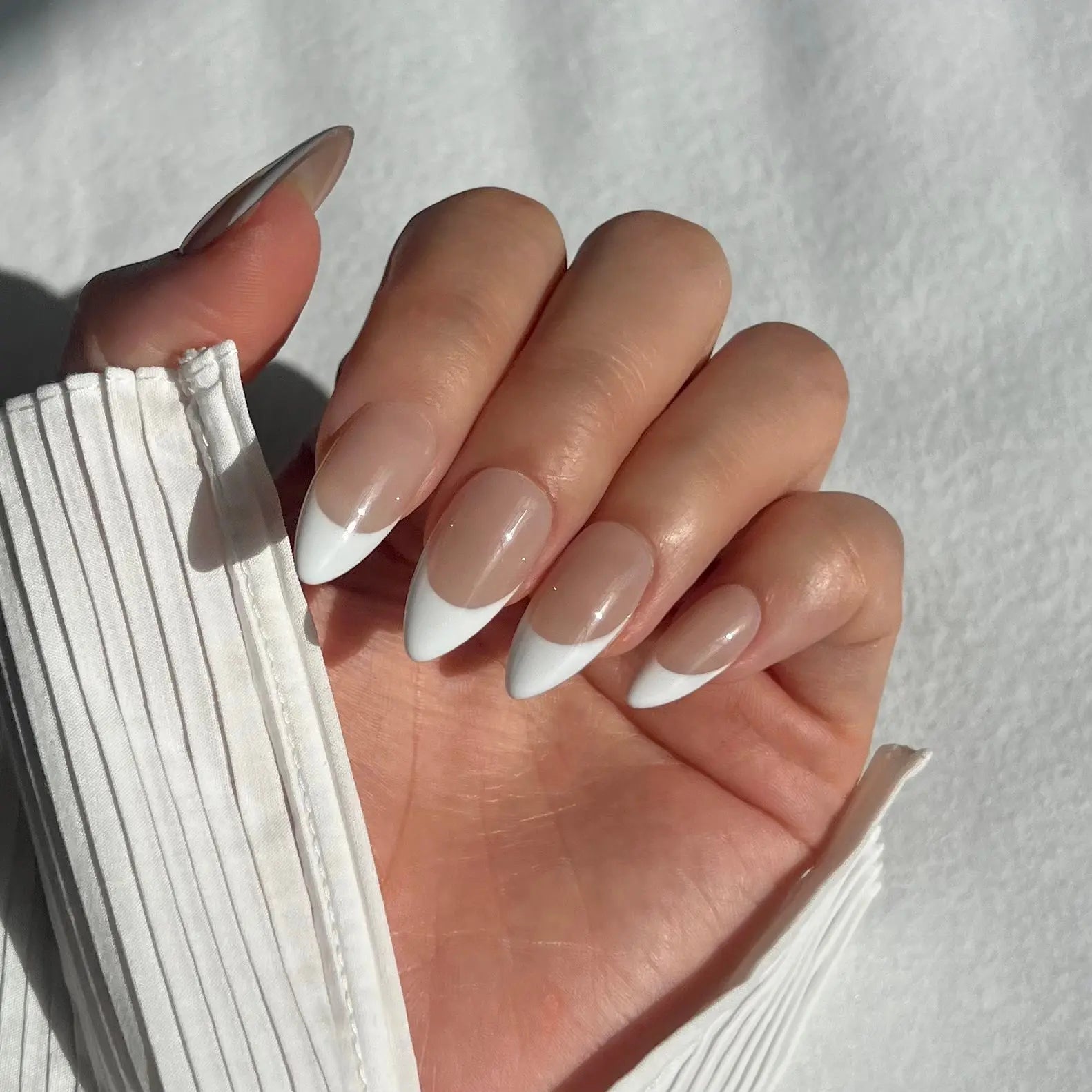 A close-up of a hand wearing almond-shaped press-on nails with a nude base and white French tips, giving a classic yet contemporary twist.