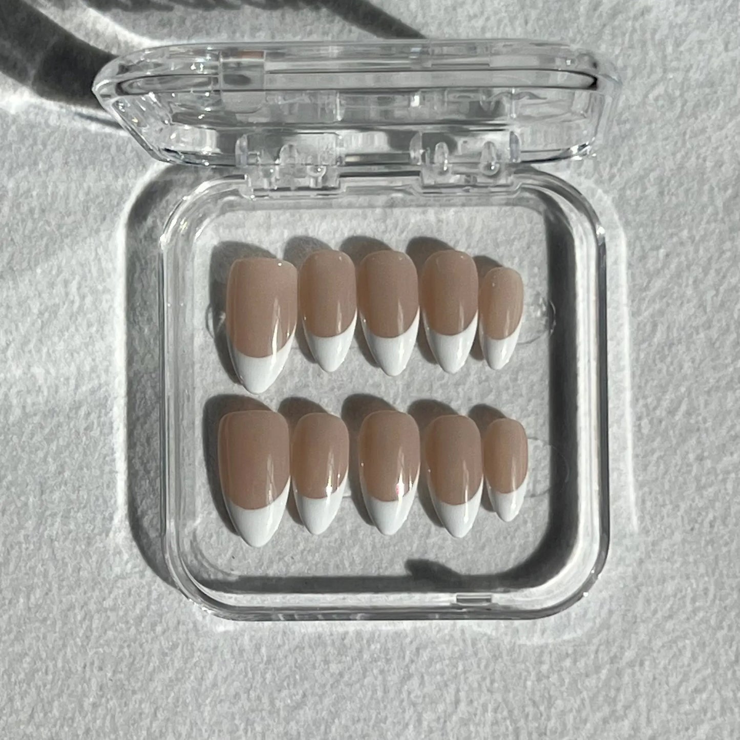 A set of press-on nails displayed in a clear plastic box, featuring a nude base with bold, curved white French tips for a modern and stylish look.