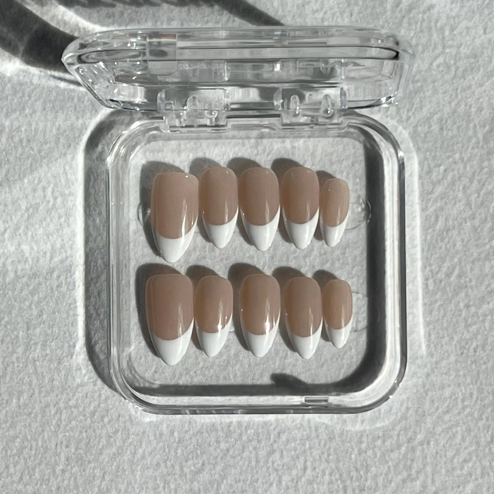 A set of press-on nails displayed in a clear plastic box, featuring a nude base with bold, curved white French tips for a modern and stylish look.